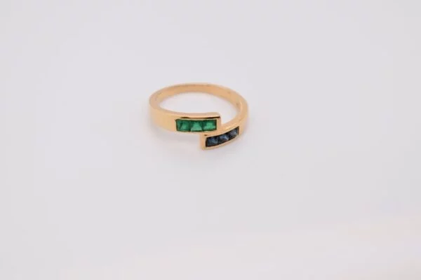 Minimalist 18K yellow gold ring adorned with square-cut natural emeralds and sapphires. Features 2x2 mm gemstones, with 3 emeralds and 3 sapphires. Size 5.75 US.