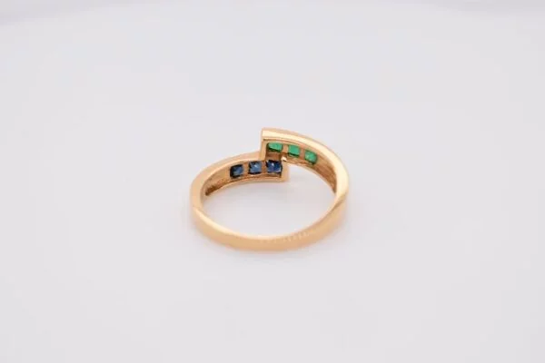 Minimalist 18K yellow gold ring adorned with square-cut natural emeralds and sapphires. Features 2x2 mm gemstones, with 3 emeralds and 3 sapphires. Size 5.75 US.