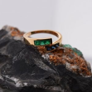 Minimalist 18K yellow gold ring adorned with square-cut natural emeralds and sapphires. Features 2x2 mm gemstones, with 3 emeralds and 3 sapphires. Size 5.75 US.