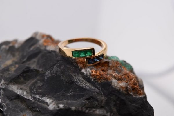 Minimalist 18K yellow gold ring adorned with square-cut natural emeralds and sapphires. Features 2x2 mm gemstones, with 3 emeralds and 3 sapphires. Size 5.75 US.