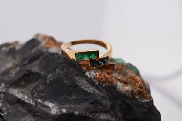 Minimalist 18K yellow gold ring adorned with square-cut natural emeralds and sapphires. Features 2x2 mm gemstones, with 3 emeralds and 3 sapphires. Size 5.75 US.